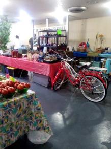 Photo of vendor table displaying miscellaneous household items and a red bicycle for sale.